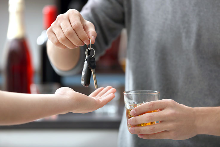Alcohol. A photo shows a person, holding a drink, handing over keys to another person.