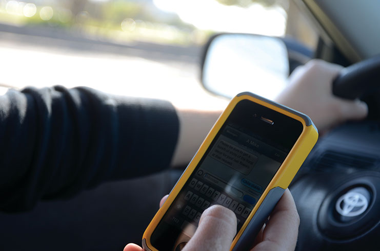 Texting. A photo shows a person holding a cell phone while driving.